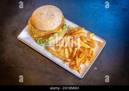 Gros plan d'un hamburger végétalien avec guacamole et frites sur une assiette blanche sur fond noir Banque D'Images