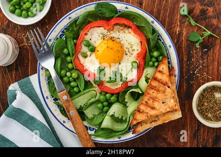 Poivrons rouges farcis avec des œufs, des feuilles d'épinards, des pois verts et des microverts sur une assiette de petit déjeuner sur fond de table en bois. Vue de dessus. Banque D'Images