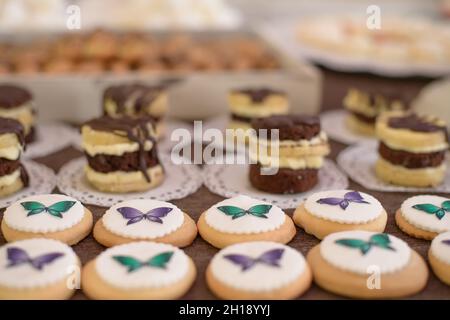 Assortiment de petits gâteaux plats aux boutons, ornés de papillons glaçant colorés vendus dans une pâtisserie ou préparés pour les anniversaires Banque D'Images
