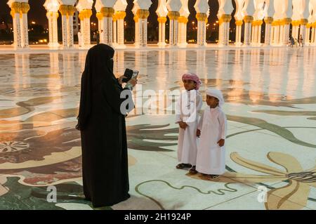 Une femme qui prend des photos de ses fils dans une robe traditionnelle avec un téléphone portable à la Grande Mosquée Sheikh Zayed.Grande mosquée Sheikh Zayed, Abu Dhabi, U Banque D'Images