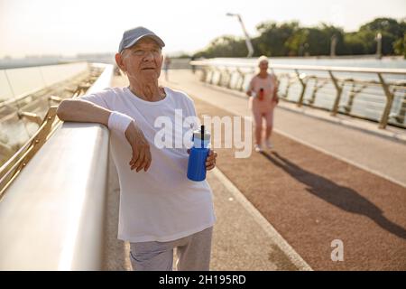 Homme mature avec repose-bouteille près de la main courante tandis que la femme court le long de la passerelle Banque D'Images