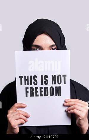 Femme musulmane tenant un papier avec du texte - ce n'est pas la liberté.Femme musulmane en vêtements hijab traditionnels.Violence domestique, discrimination des musulmans Banque D'Images