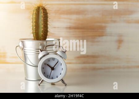 Réveil blanc avec cactus en pot sur un bureau en bois.Concept de temps minimal. Banque D'Images