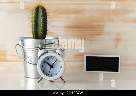 Réveil blanc avec cactus en pot sur un bureau en bois.Concept de temps minimal. Banque D'Images