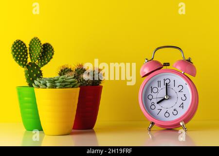 Réveil rose avec cactus en pot sur un bureau en bois.Concept de temps minimal. Banque D'Images