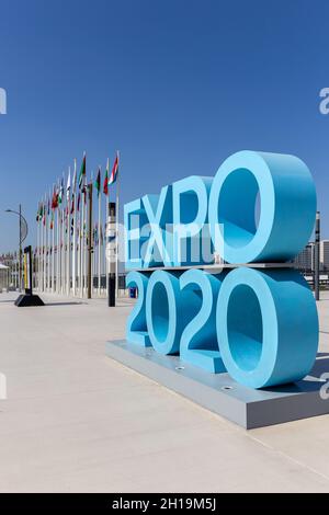 Dubaï, Émirats arabes Unis, 17.10.2021.Affiche du logo bleu de l'Expo 2020 à l'entrée du quartier de la mobilité du site de l'Expo avec drapeaux nationaux des participants en arrière-plan. Banque D'Images