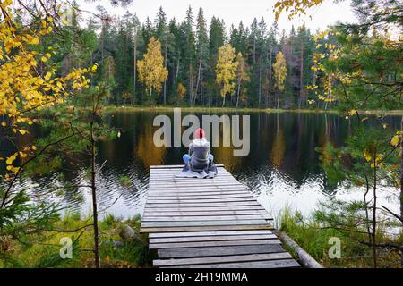 Une jeune femme s'assoit sur le quai en admirant le paysage de la forêt d'automne, lac avec des arbres dorés jaunes colorés Banque D'Images