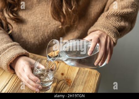 Une femme verse de l'eau dans un verre à partir d'une carafe en verre. Banque D'Images