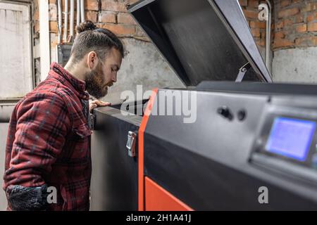 L'homme regardant dans une chaudière sur combustible solide dans la chambre avec des granulés. Banque D'Images