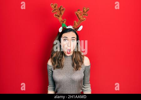 Jeune fille hispanique portant un chapeau de noël cerf effrayé et étonné de la bouche ouverte pour la surprise, le visage incrédulé Banque D'Images