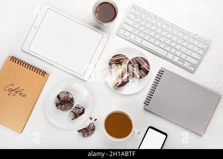 Composition avec une tasse de café, un ordinateur portable, une tablette et des beignets sur fond clair Banque D'Images