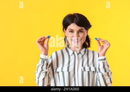 Femme mûre avec des bouchons d'oreille bleus sur fond jaune Banque D'Images