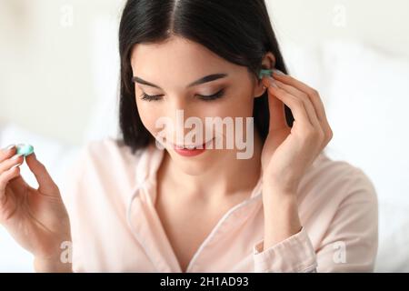 Jolie jeune femme mettant le bouchon d'oreille bleu dans la chambre, gros plan Banque D'Images