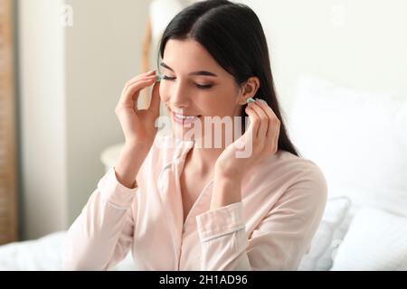 Jolie jeune femme mettant des bouchons d'oreille bleus dans la chambre Banque D'Images