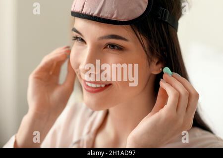 Jolie jeune femme mettant des bouchons d'oreille bleus dans la chambre, gros plan Banque D'Images