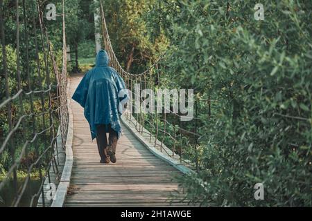 Fille avec sac à dos sous imperméable bleu est engagé dans la randonnée.Pont de suspension Banque D'Images