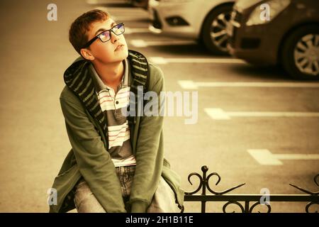 Triste adolescent dans le pull à capuche vert assis sur la main courante Banque D'Images