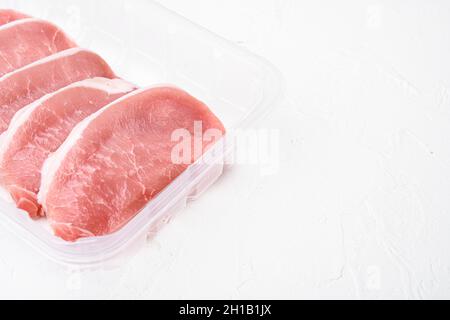 Viande de porc.Ensemble de steaks de porc frais, dans un emballage en plastique, sur fond de table en pierre blanche, avec espace pour le texte Banque D'Images