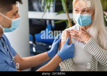 Senior Lady se faire vacciner contre Covid, infirmière appliquant le bandage adhésif Banque D'Images