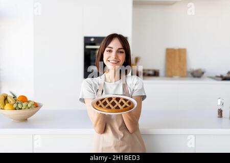 Dessert maison.Bonne dame tenant et montrant la tarte fraîchement cuite, portant un tablier et préparant la pâtisserie dans la cuisine Banque D'Images