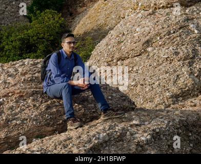 Jeune indien avec sac à dos assis sur le rocher regardant la nature autour de lui. touriste reposant sur le chemin de la montagne Banque D'Images