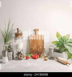 Cuisine domestique sans déchets fond de vie avec pots en verre, planche à découper en bois, plantes, ustensiles en verre, mortier et pilon sur table gris pâle Banque D'Images