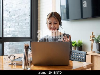 Prise de vue rognée femme asiatique souriante freelancer portant un casque, communiquant avec le client via un appel vidéo sur ordinateur.Professionnel agréable millénaire Banque D'Images