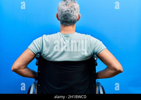 Beau homme d'âge moyen aux cheveux gris assis sur un fauteuil roulant debout en arrière et regardant loin avec les bras sur le corps Banque D'Images