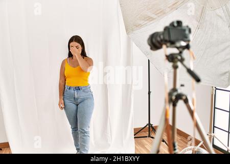 Jeune belle femme hispanique posant comme modèle au studio de photographie fatigué frottant nez et yeux sensation de fatigue et de maux de tête. Stress et frustration Banque D'Images