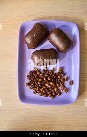 Trois chocolats et une poignée de grains de café se trouvent sur une assiette mauve.Vue de dessus.Gros plan Banque D'Images