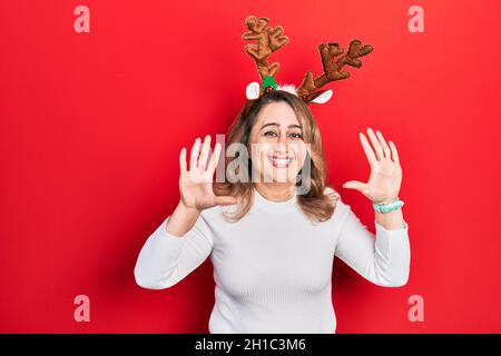 Femme caucasienne d'âge moyen portant de mignons cornes de renne de noël montrant et pointant vers le haut avec les doigts numéro dix tout en souriant confiant et heureux. Banque D'Images