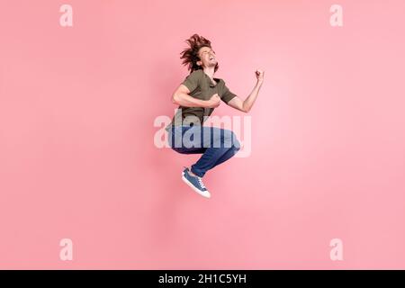 Pleine longueur profil photo de côté de jeune homme saut célébrer la victoire choqué gagner loterie isolée sur fond de couleur rose Banque D'Images