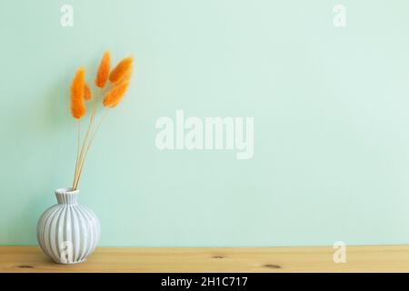 Vase d'orange lièvres queue herbe fleurs sèches sur table en bois. Fond de mur menthe. Espace de copie Banque D'Images