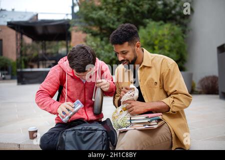 Jeune homme étudiant avec le syndrome de Down et son ami de mentorat assis à l'extérieur dans la zone du campus Banque D'Images