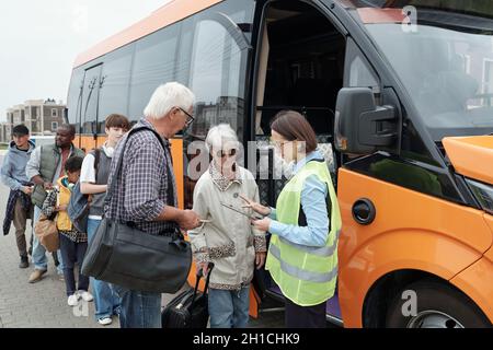 Un conducteur de bus vérifie les billets des passagers interculturels debout le long du véhicule Banque D'Images