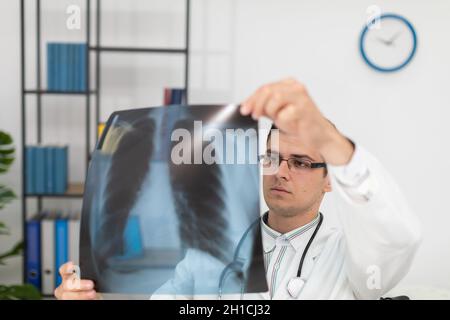 Un pneumologue dans son cabinet médical vérifie d'abord la radiographie pulmonaire de son patient. Banque D'Images