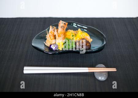 Deux crevettes en pâte avec sauce et champignons sur l'assiette noire.Crevettes frites au décor de verdure et de fleurs. Baguettes en bois Banque D'Images
