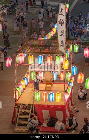 Vue sur la place en face de la gare de Nippori décorée pour le festival d'Obo avec une tour yagura illuminée de lanternes en papier où un g Banque D'Images