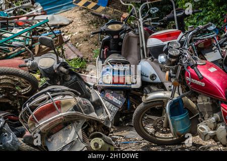 Yangshuo, Chine - Août 2019 : Utilisé, vieux, endommagé et mis au rebut des motos, motos et scooters empilés dans la cour à l'extérieur du recyclage des métaux p Banque D'Images