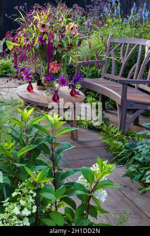 Contemplez le stand Burvill.Vase exubérant de fleurs coupées sur une table basse en bois devant un banc en bois incurvé.Les fleurs comprennent dahlia, échinacée, Amaranthus c Banque D'Images