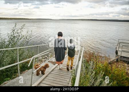 Vue arrière de la mère marchant le long du pont vers le lac avec son fils et son chien Banque D'Images