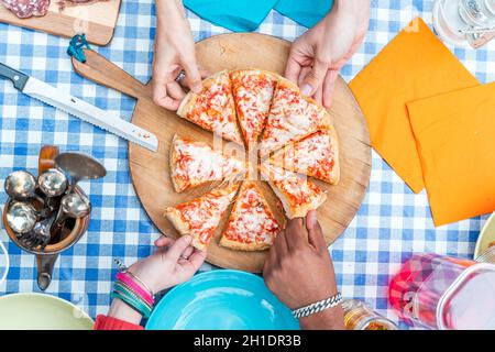 groupe d'amis qui mangent de la pizza.Vue de dessus de quatre mains prenant des tranches de pizza de planche à découper en bois Banque D'Images
