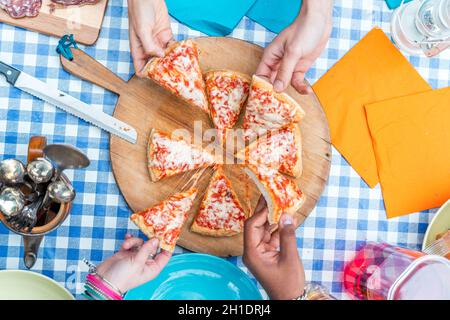 groupe d'amis qui mangent de la pizza.Vue de dessus de quatre mains prenant des tranches de pizza de planche à découper en bois Banque D'Images