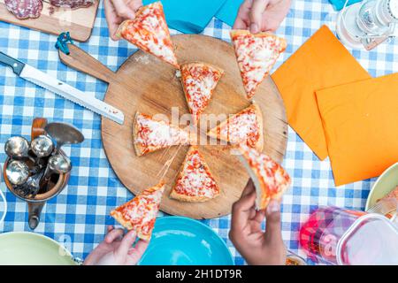 groupe d'amis qui mangent de la pizza.Vue de dessus de quatre mains prenant des tranches de pizza de planche à découper en bois Banque D'Images