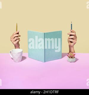 Concept de bureau original avec carnet ouvert droit flanqué par les mains d'un homme tenant un stylo et un crayon avec la tête cachée derrière les pages, une tasse de café et Banque D'Images
