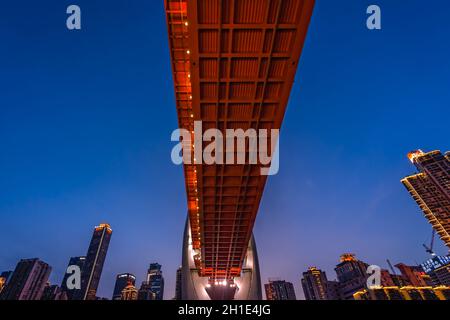 Chongqing, Chine - août 2019 : pont routier éclairé DongShuiMen sur et en traversant la puissante rivière Yangtze dans la ville de Chongqing au crépuscule Banque D'Images