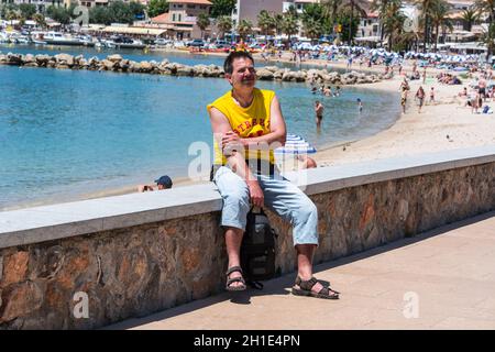 Paguera, MALLORCA, ESPAGNE - 02 JUILLET 2016: Paguera, Mallorca, Espagne - 02 juillet 2016: Un homme assis au soleil sur un mur dans le pin de fond pour Banque D'Images