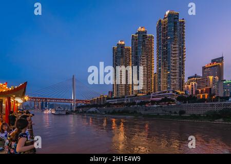 Chongqing, Chine - Août 2019 : passagers sur la terrasse d'observation du bateau touristique de la ville en admirant la vue nocturne sur le commerce et le bus modernes Banque D'Images