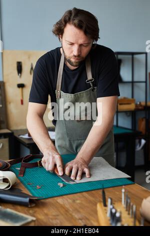Portrait vertical d'un homme barbu artisan travaillant avec le cuir en atelier, concept de petite entreprise Banque D'Images