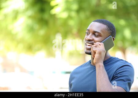 Un homme heureux avec une peau noire parlant sur un téléphone portable dans un parc Banque D'Images